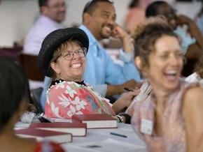 LTSS professors and alumni smiling and laughing around tables during an event.