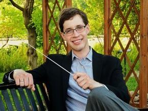 Tyler Stark holding conducting baton while sitting on a park bench